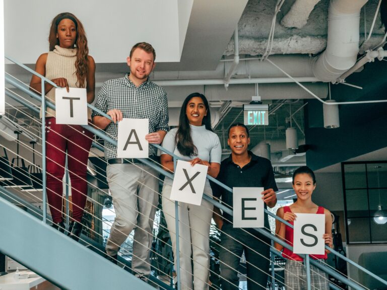 A diverse group of professionals smiling and holding 'TAXES' signs on an indoor stairway